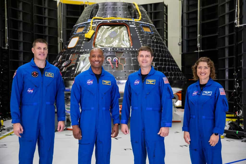 Quatro astronautas da missão Artemis II, vestindo macacões azuis de voo da NASA, posam em frente ao módulo espacial Orion dentro de um hangar. Da esquerda para a direita: Jeremy Hansen, Victor Glover, Reid Wiseman e Christina Hammock Koch.