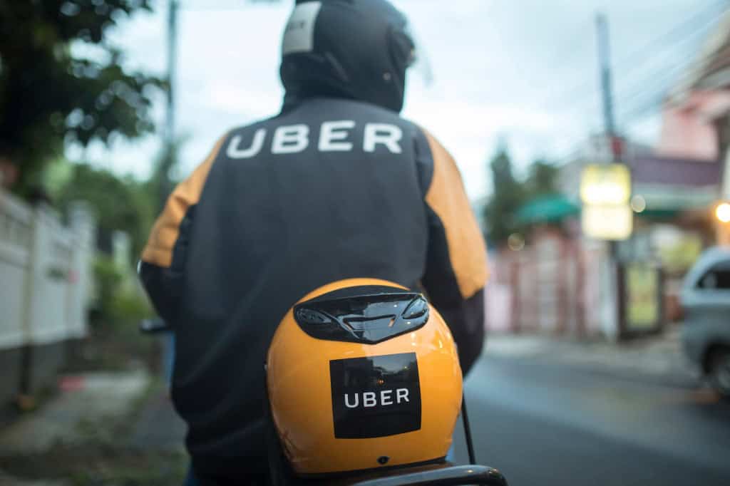 Motociclista da Uber usando um capacete de costas em cima de uma moto, com um capacete atrás