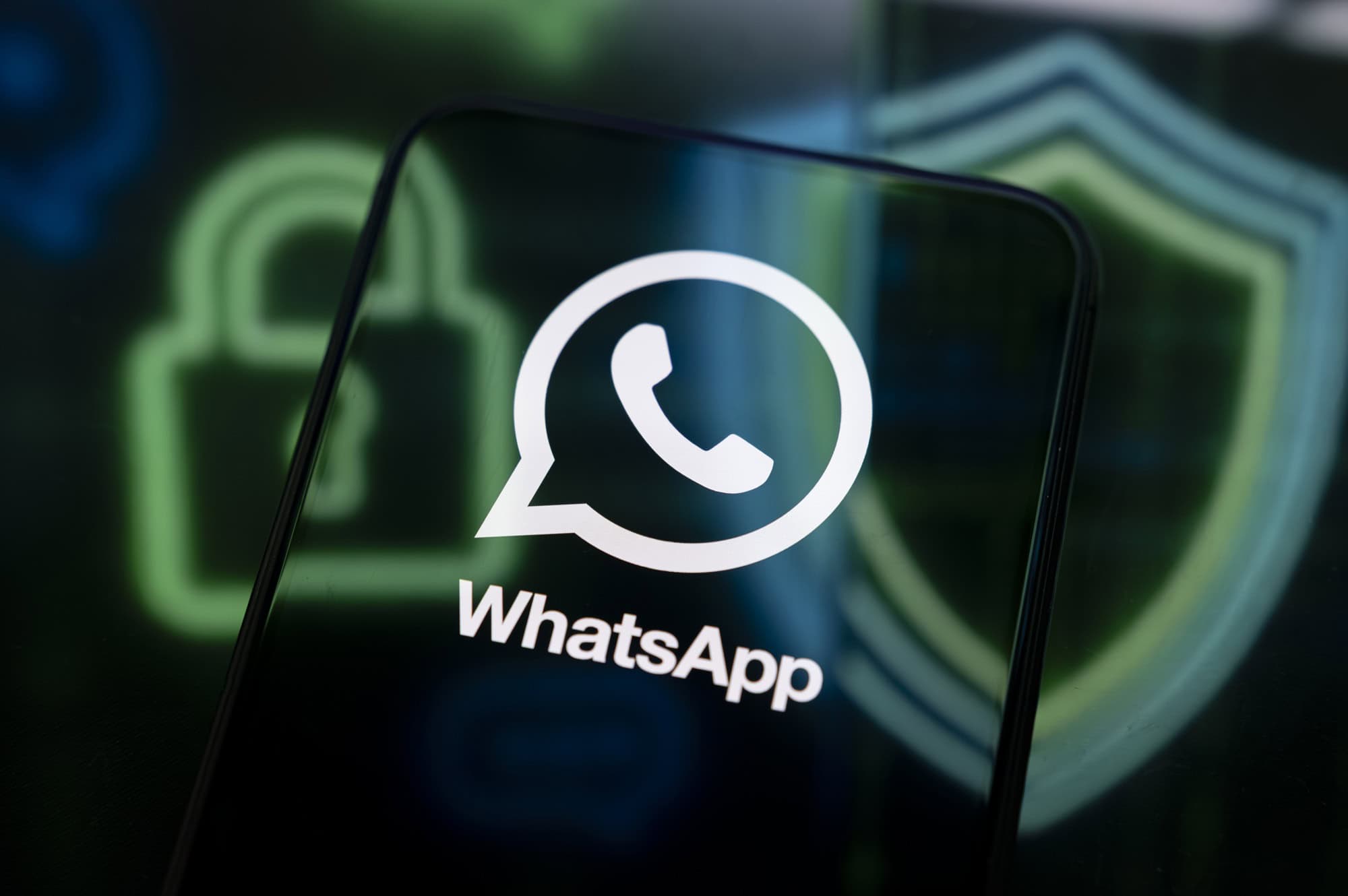 Logo do WhatsApp exibido na tela de um smartphone, com ícones de cadeado e escudo desfocados ao fundo