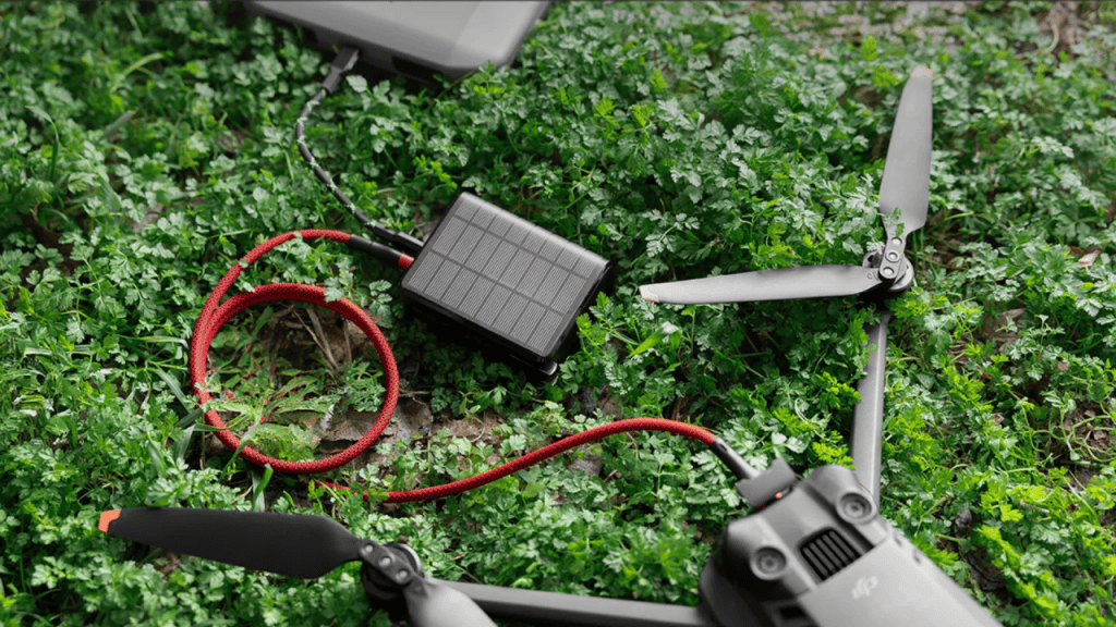 Power bank carregando um drone e seu controle. Os equipamentos estão sob a grama