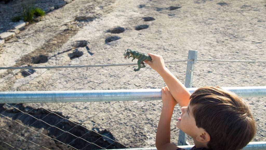 Criança brinca com brinquedo de dinossauro perto de pegadas de dinossauro