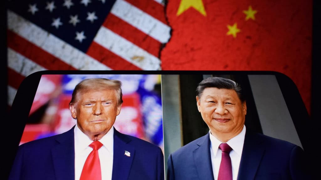 Celular exibe fotos de Donald Trump e Xi Jinping enquanto monitor exibe, ao fundo, montagem com bandeiras dos Estados Unidos e da China