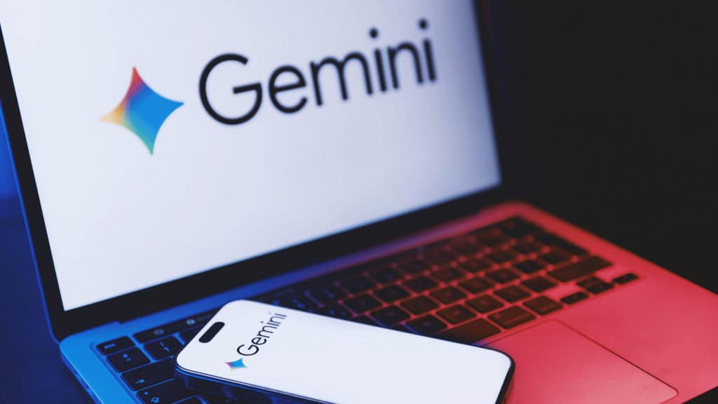 Celular colocado sobre teclado de notebook; ambos exibem logomarca do Google Gemini nas suas telas