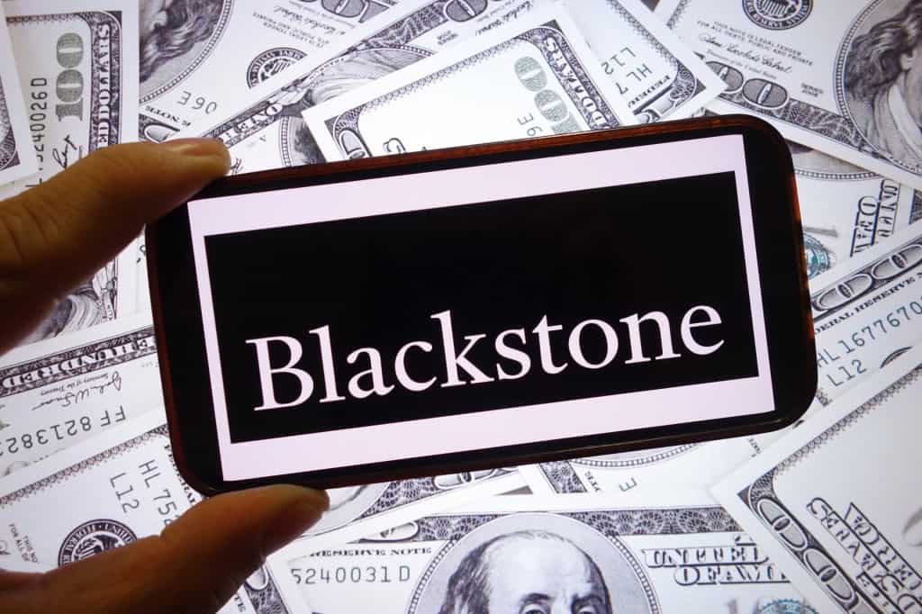 Logo da Blackstone em um smartphone; atrás, várias notas de dólar