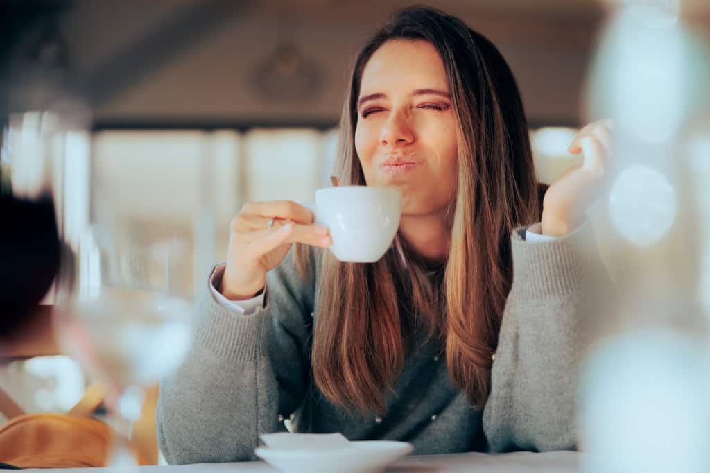 Mulher faz expressão de amargor enquanto toma uma xícara de café em cafeteria