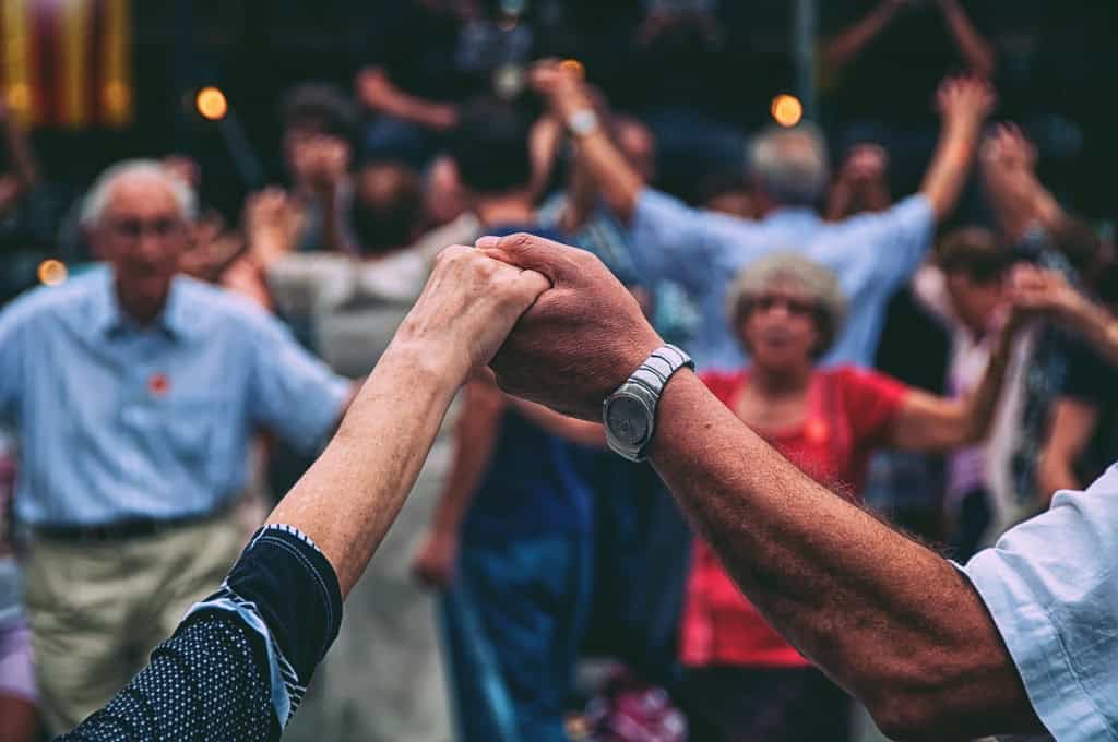 Pessoas idosas dançam de mãos dadas durante atividade coletiva em ambiente fechado