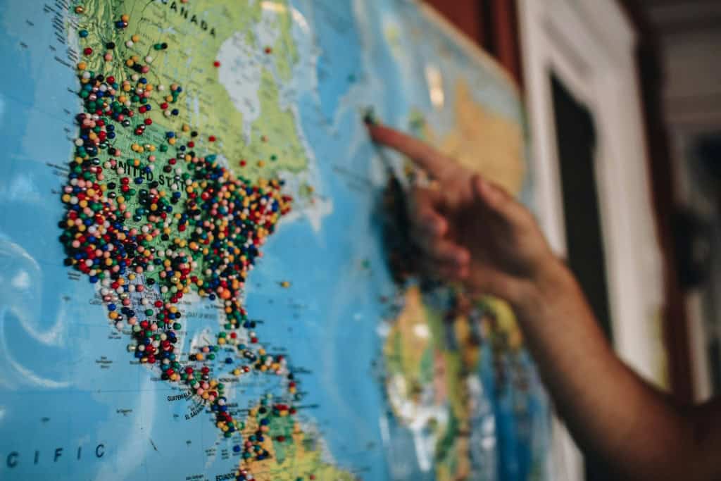 foto do mapa mundi em uma parede enquanto vários alfinetes estão presentes em diferentes regiões