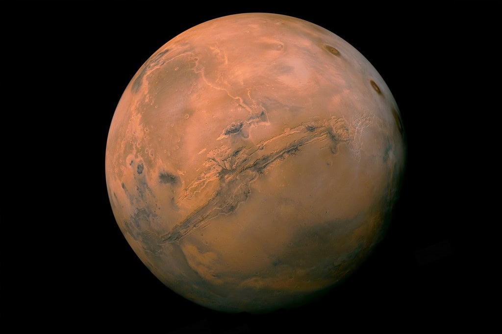 Imagem de Marte mostrando a superfície avermelhada do planeta, com destaque para o sistema de cânions Valles Marineris atravessando a região central.