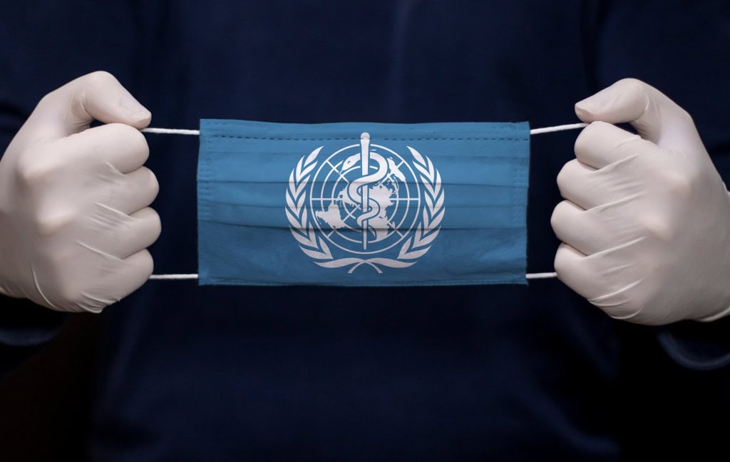 máscara com o símbolo da organização mundial da saúde segurada por duas mãos com luvas de procedimento