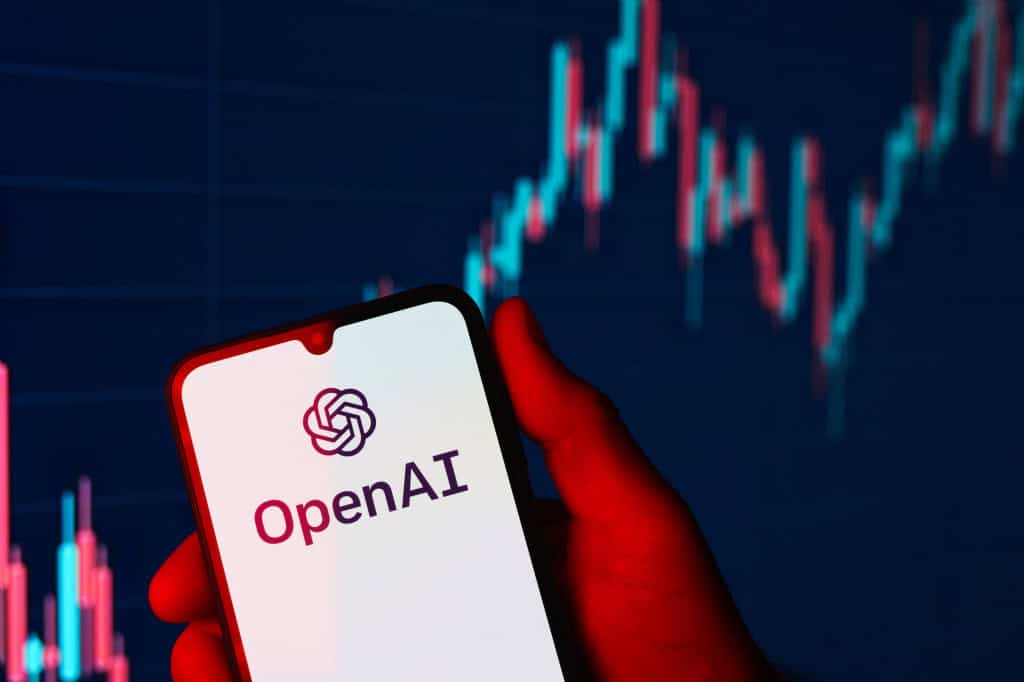 Ao fundo, gráfico financeiro; à frente, o logo da OpenAI em um smartphone