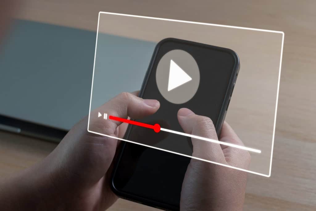 Mãos segurando um smartphone com um player de vídeo projetado acima