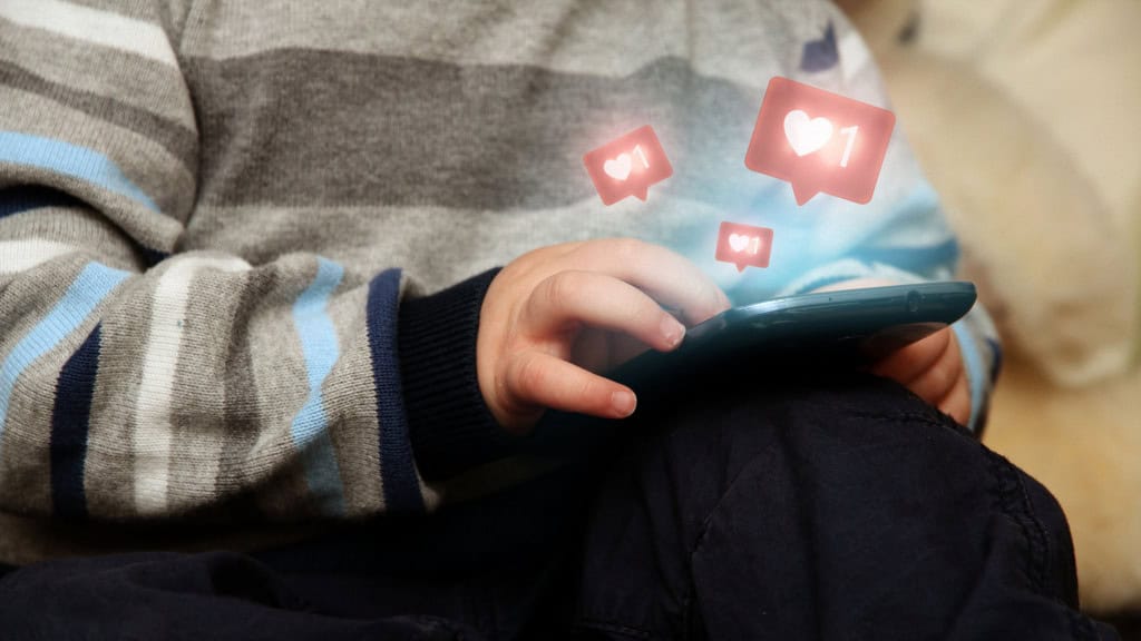 Montagem mostrando criança usando celular enquanto recebe curtidas em rede social