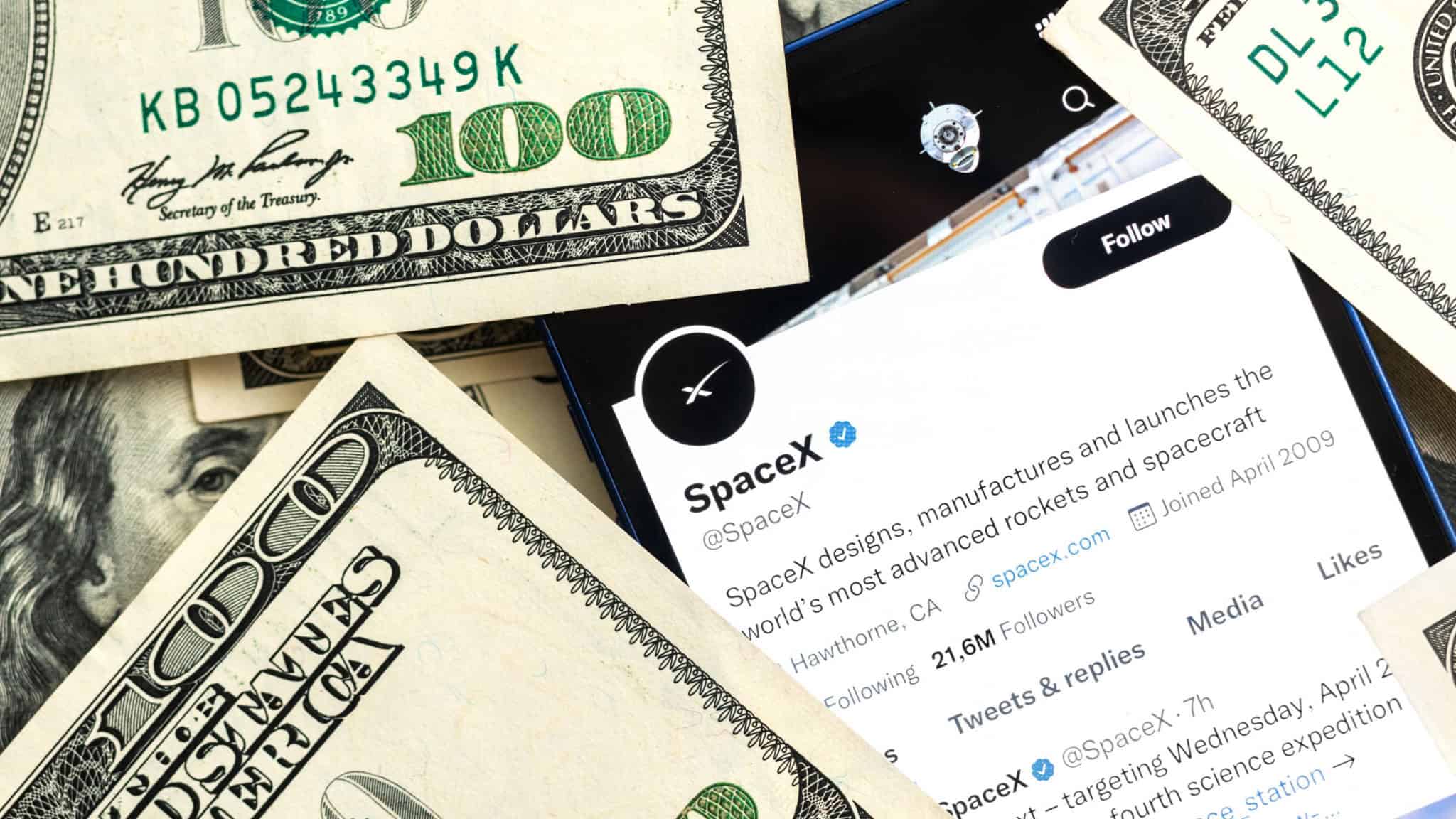 Página da SpaceX no Twitter aberta em celular rodeado de notas de dólar numa mesa