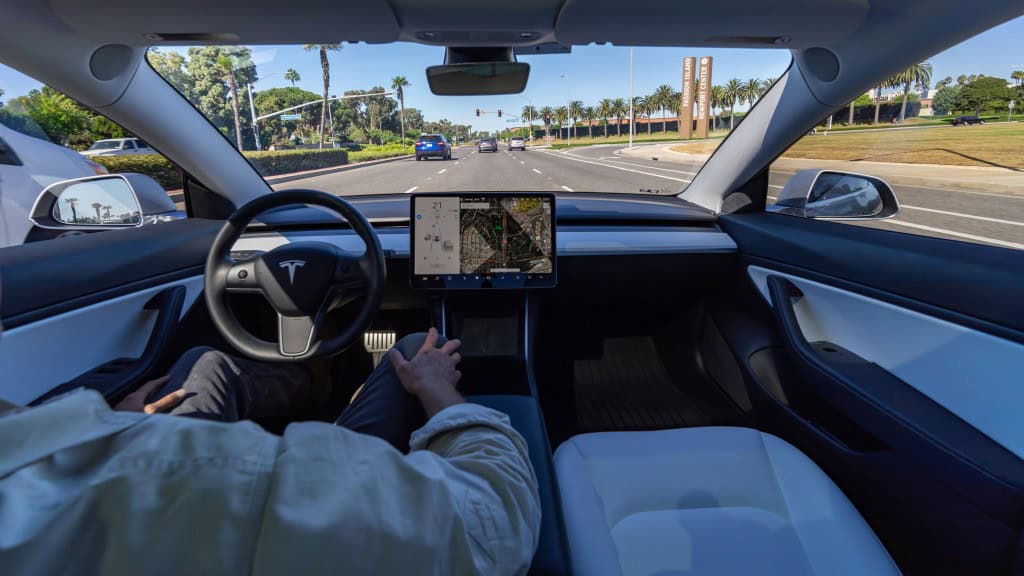 Homem com as mãos no colo enquanto anda, no banco do motorista, num carro da Tesla com sistema Full Self-Driving (FSD)