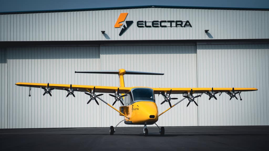 Logo da Electra em um galpão; abaixo, um avião amarelo