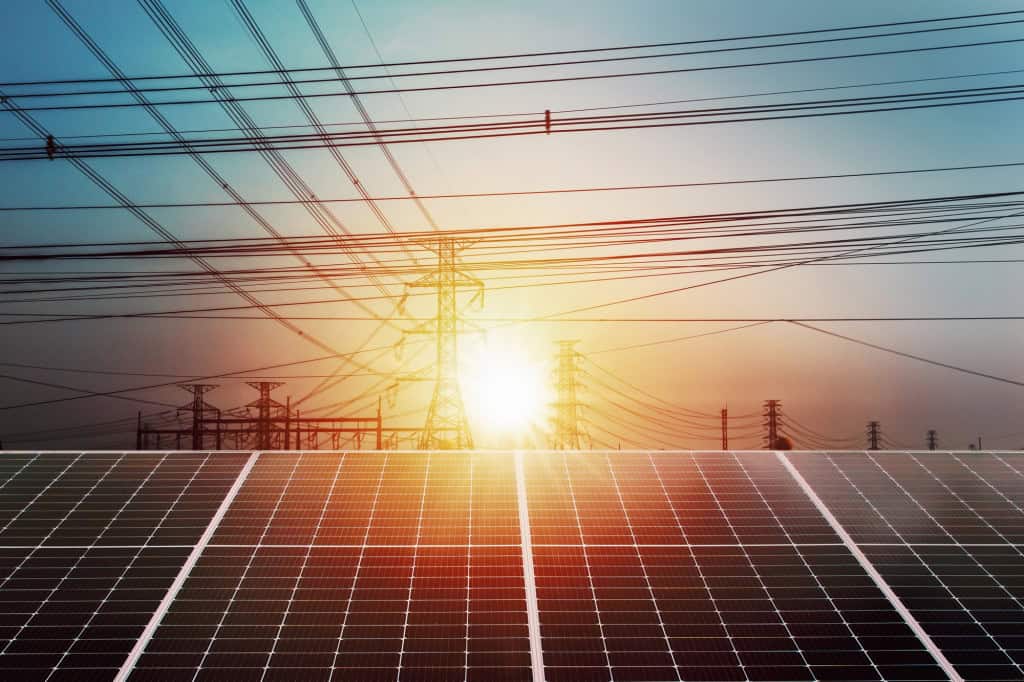 Painéis solares em primeiro plano e linhas de transmissão de alta tensão ao fundo, representando a integração da geração de energia renovável ao sistema elétrico.