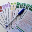 cartelas para fazer jogos das loterias caixa, com uma caneta em cima