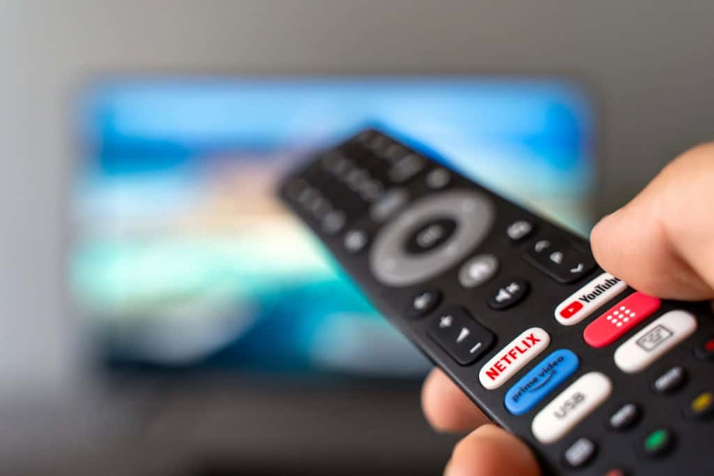 Controle remoto apontado para uma televisão com interface de streaming desfocada ao fundo.