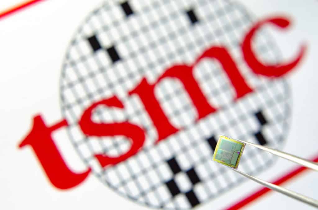 logo da tsmc ao fundo com um chip sendo segurado por uma pinça em primeiro plano