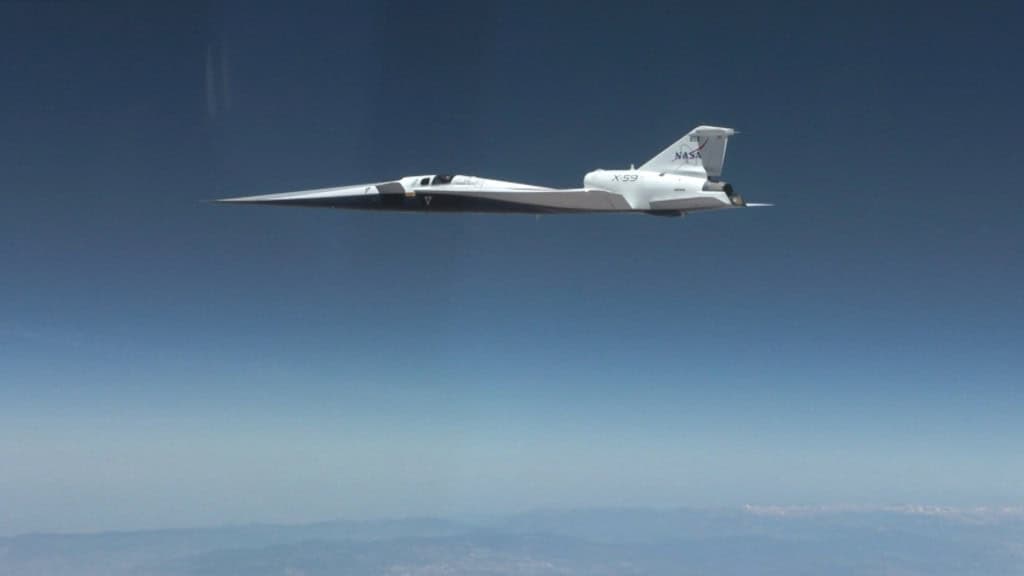 O X-59, avião experimental da NASA para pesquisas de voo supersônico silencioso, aparece em voo contra um céu azul durante seu primeiro teste acima da velocidade do som.