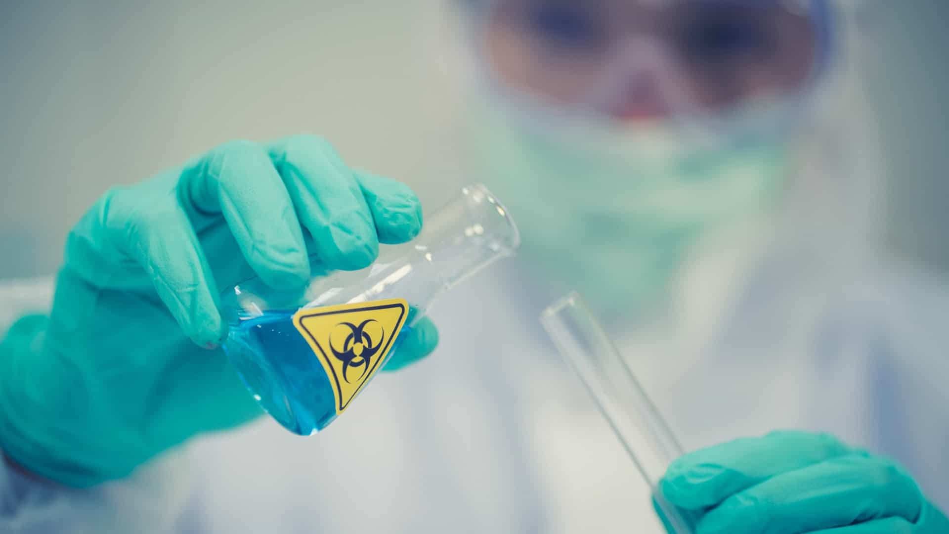 Pesquisador manipula frasco com amostra biológica em laboratório de biossegurança durante análise de agentes infecciosos.