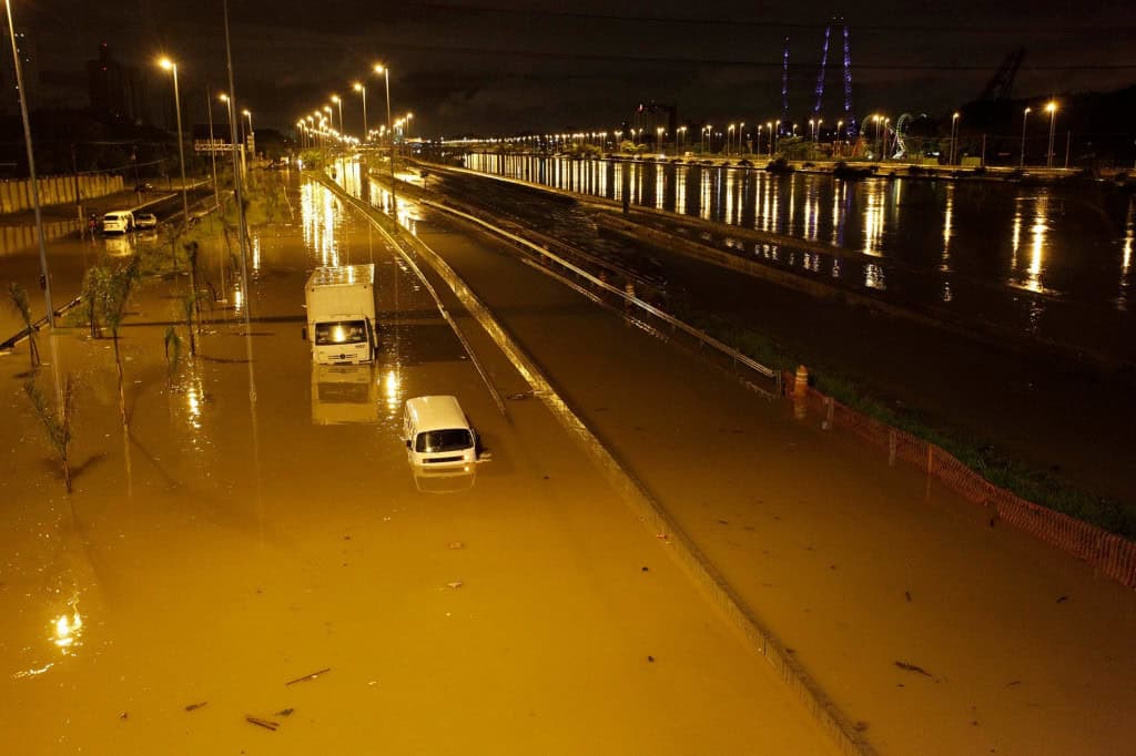 Via urbana alagada durante enchente, com veículos parcialmente submersos.
