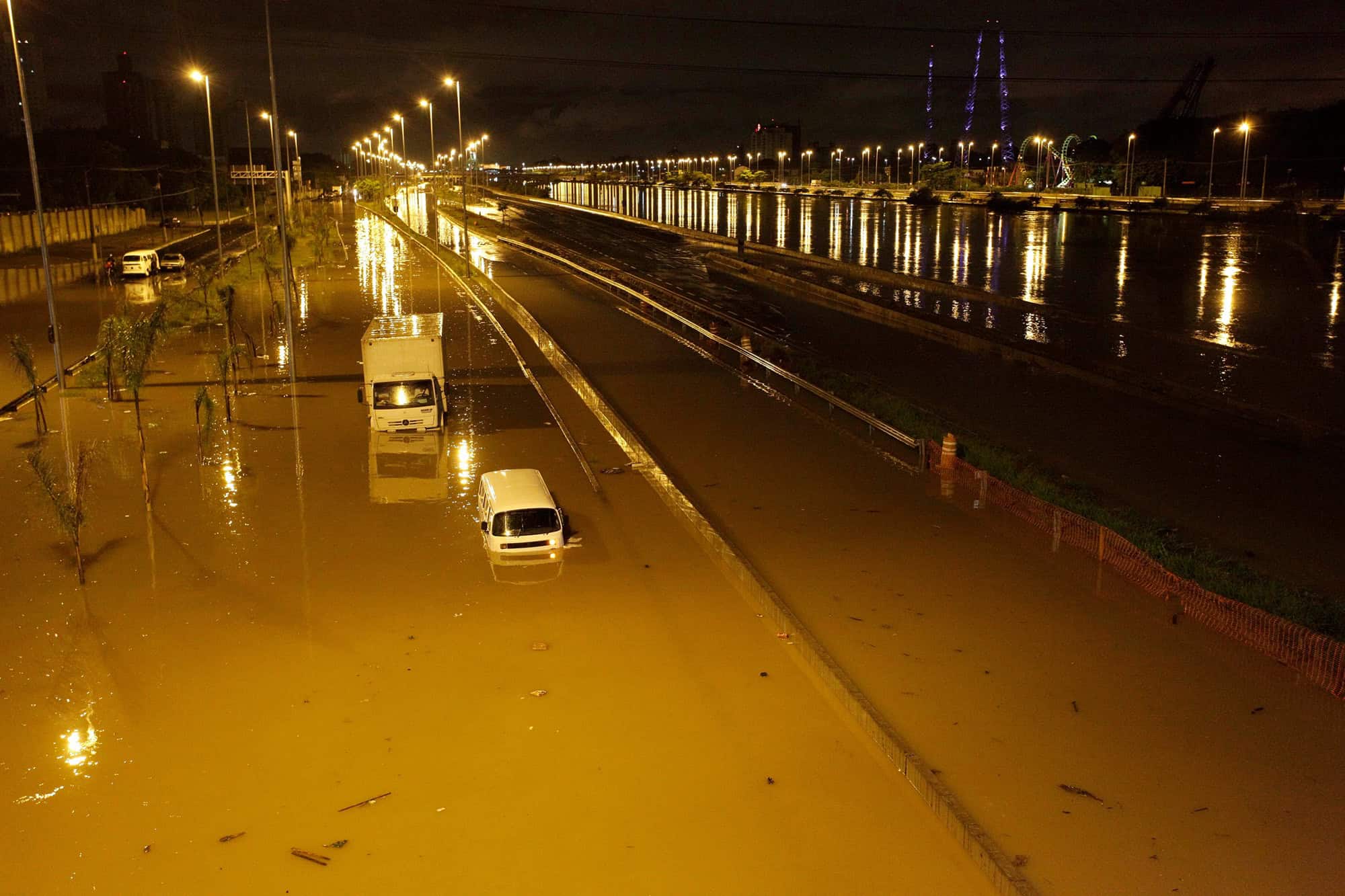 Via urbana alagada durante enchente, com veículos parcialmente submersos.