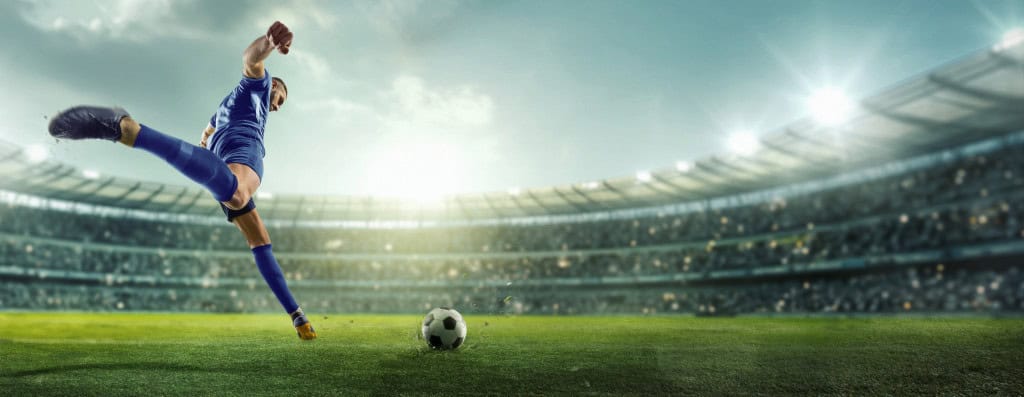 Jogador de futebol chutando uma bola em um estádio lotado.