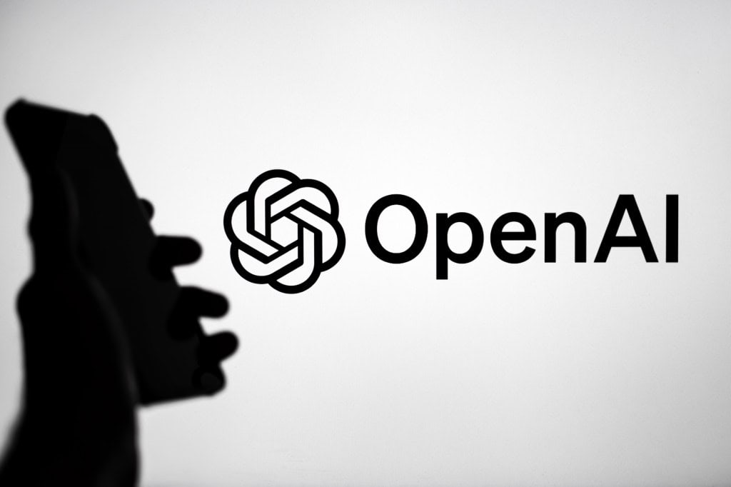 Logo da OpenAi projetado ao lado da sombra de uma mão segurando um smartphone