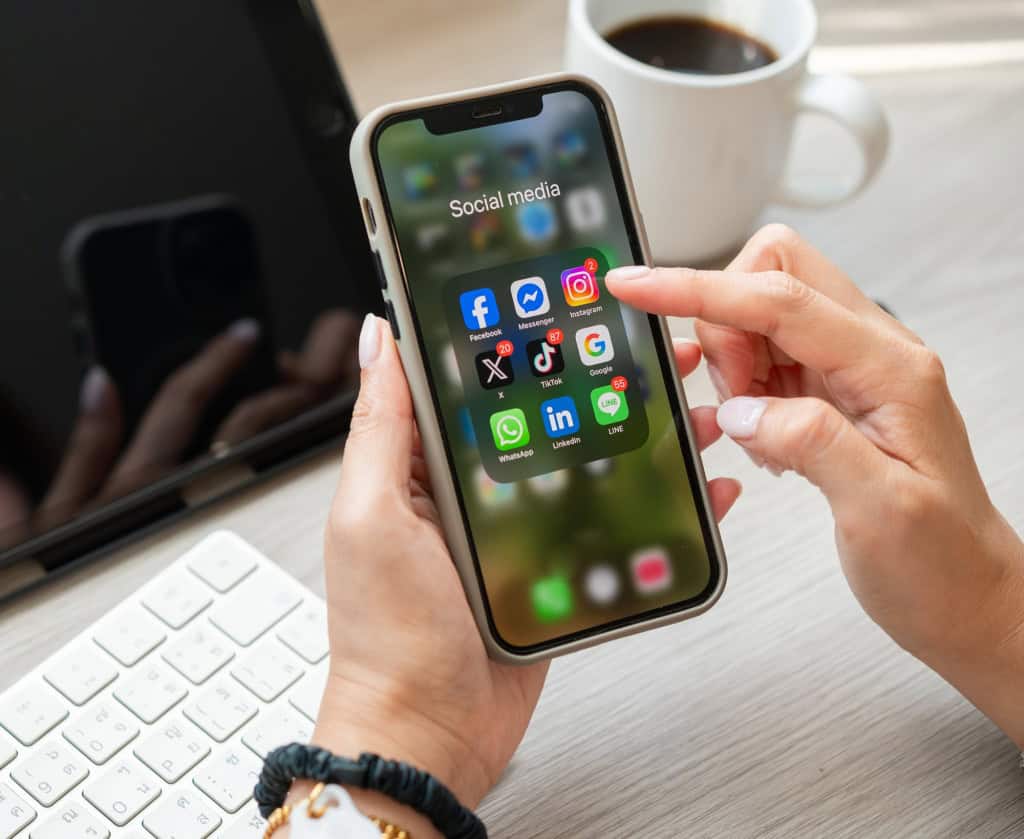 União Europeia quer definir idade mínima para acesso de crianças às redes sociais 3 Pessoa segurando um smartphone com aplicativos de redes sociais, ilustrando o uso de plataformas que utilizam algoritmos para recomendar conteúdos.