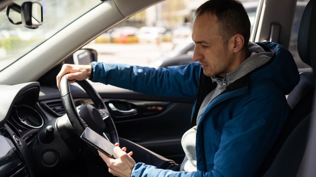 Motorista de Uber em carro; homem segura volante com uma mão e celular com a outra