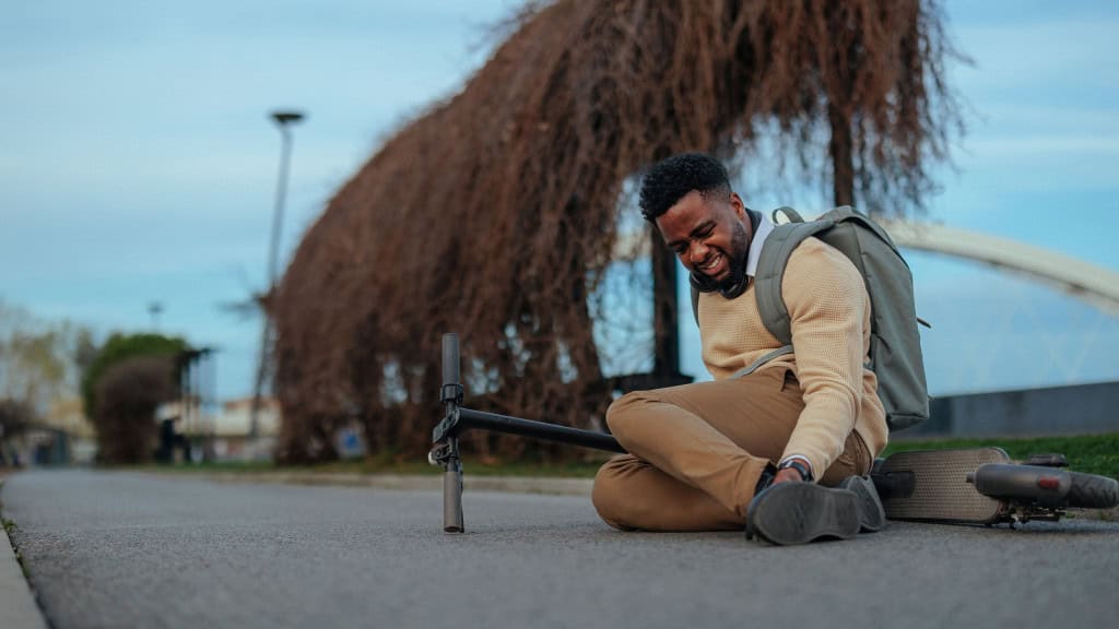 Homem sentado na rua, com cara de dor, após cair de patinete elétrico