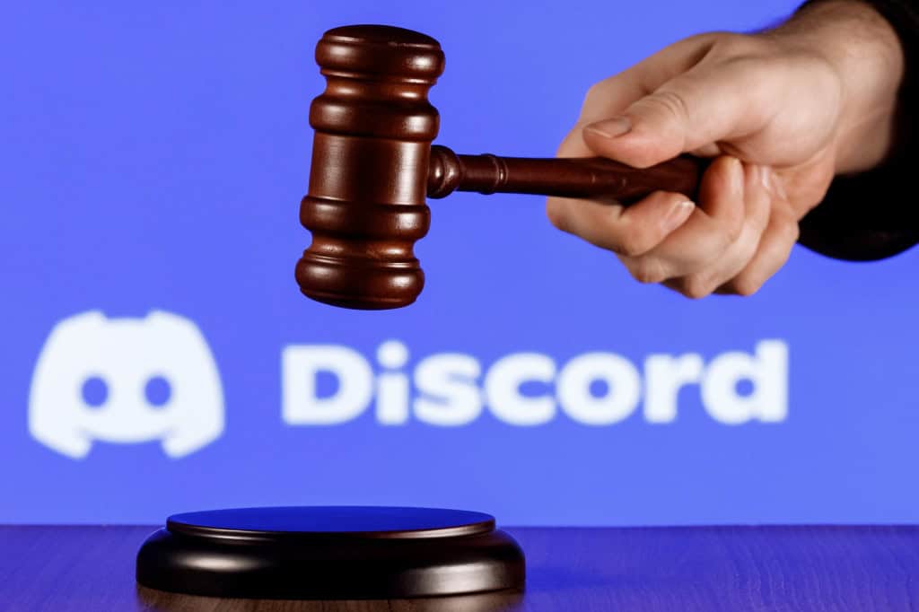 Ao fundo, logo do Discord; à frente, martelo de juiz na mão de uma pessoa