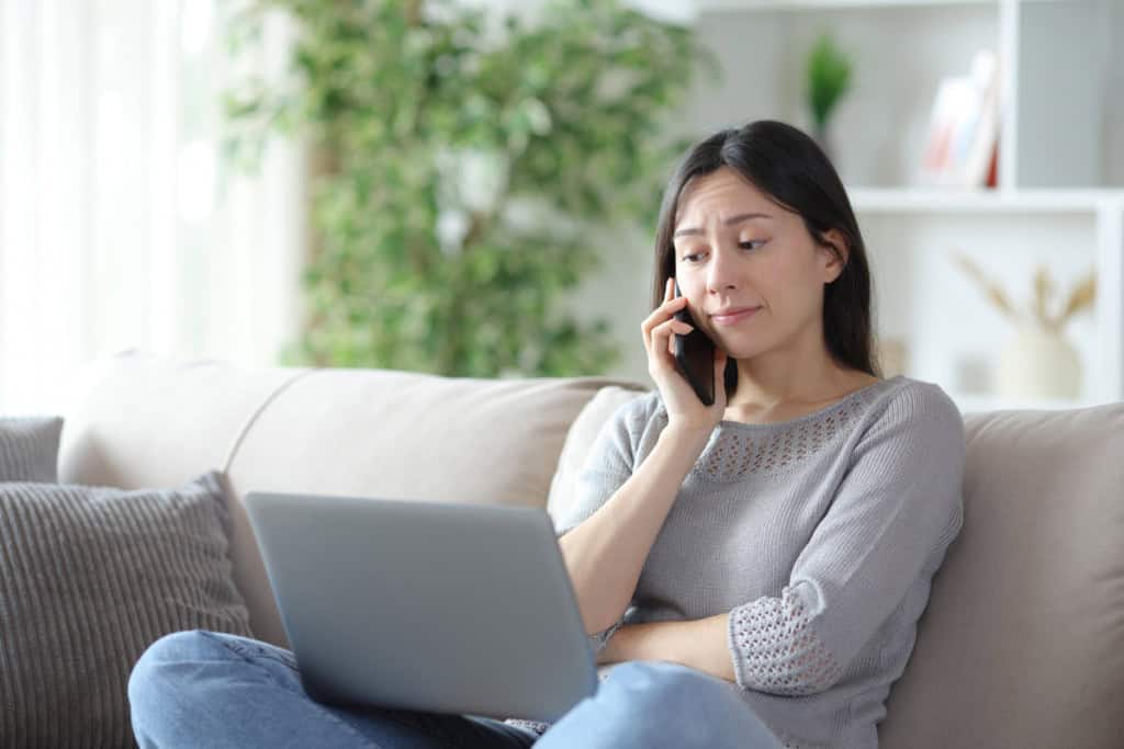 Mulher asiática decepcionada fazendo telefonema sentada em um sofá em casa