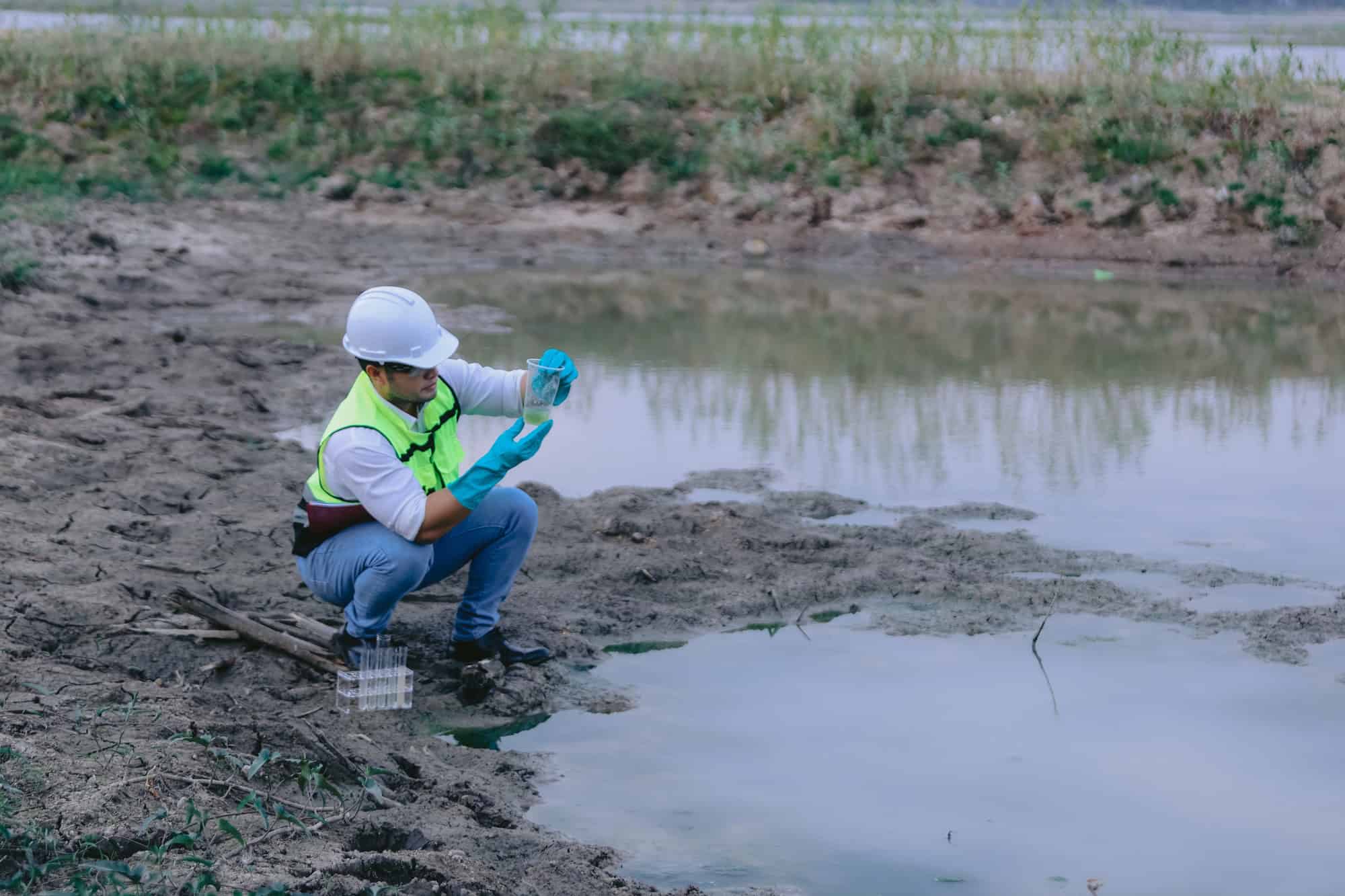 Pesquisador usando equipamentos de proteção coleta uma amostra de água em uma área natural.