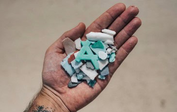 Hand holding assorted pieces of beach plastic debris highlighting environmental impact.