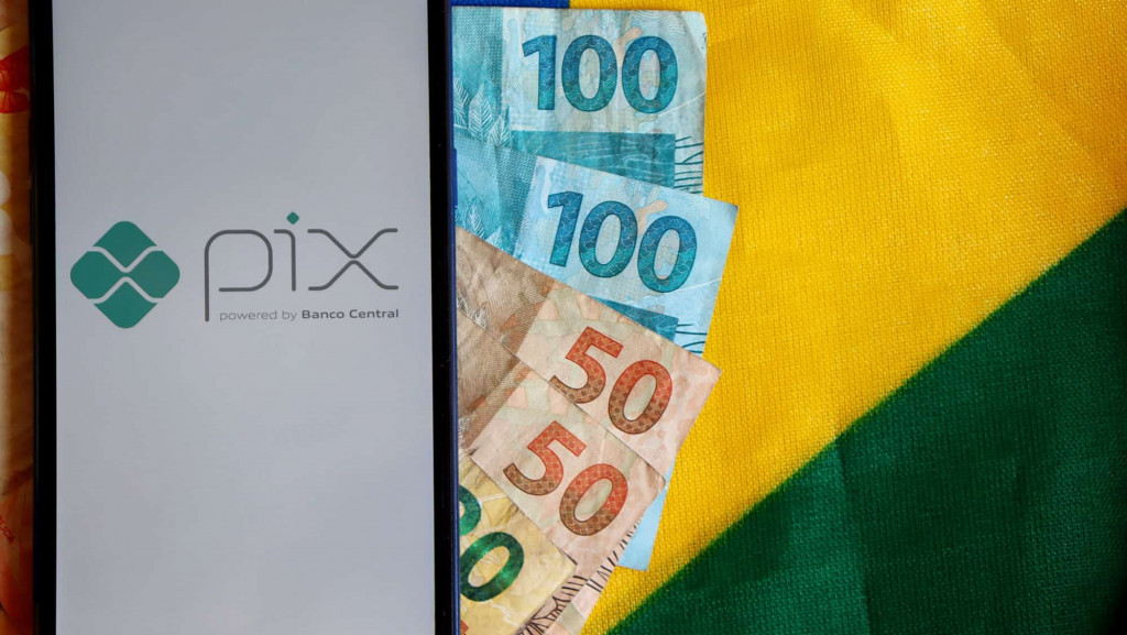 Celular com o logotipo do Pix sobre notas de reais e a bandeira brasileiras