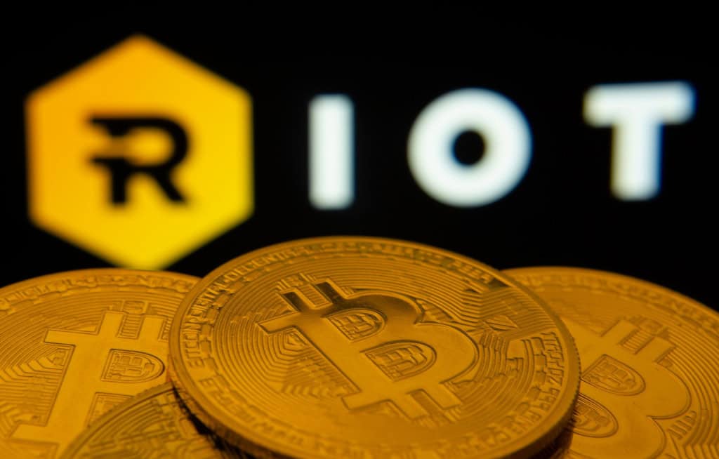 Logo da Riot Platforms com moedas de Bitcoin em contraste