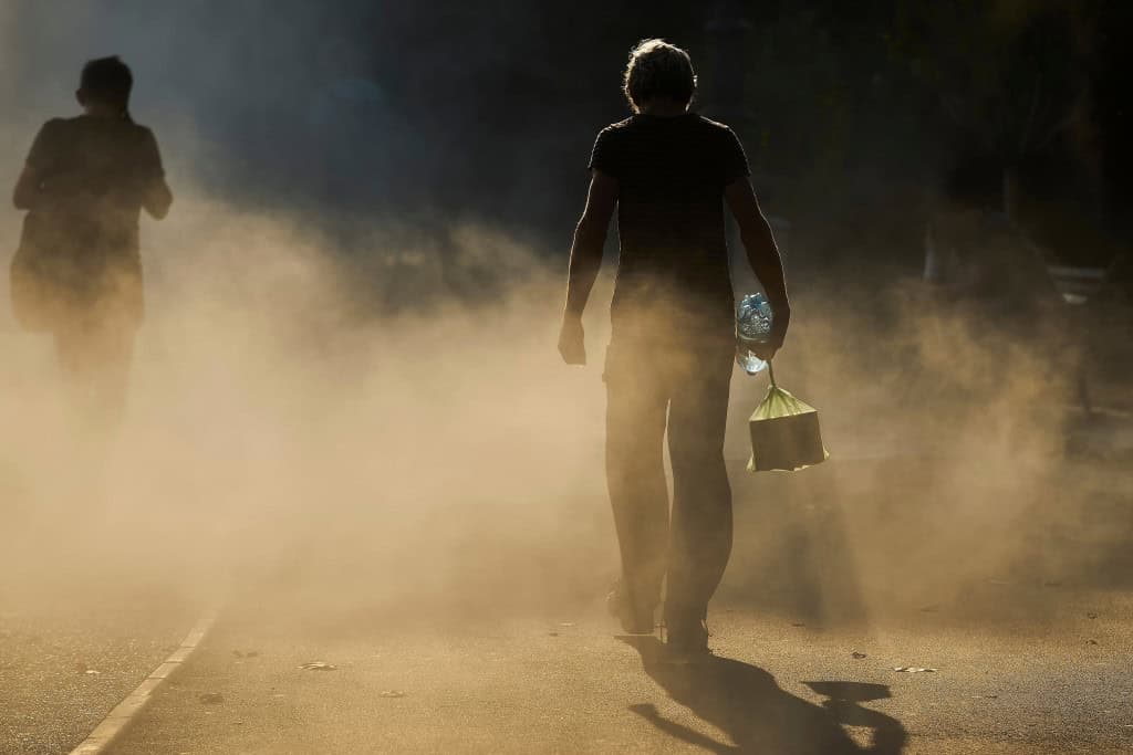 Pessoas caminham sob forte calor e poeira em uma rua
