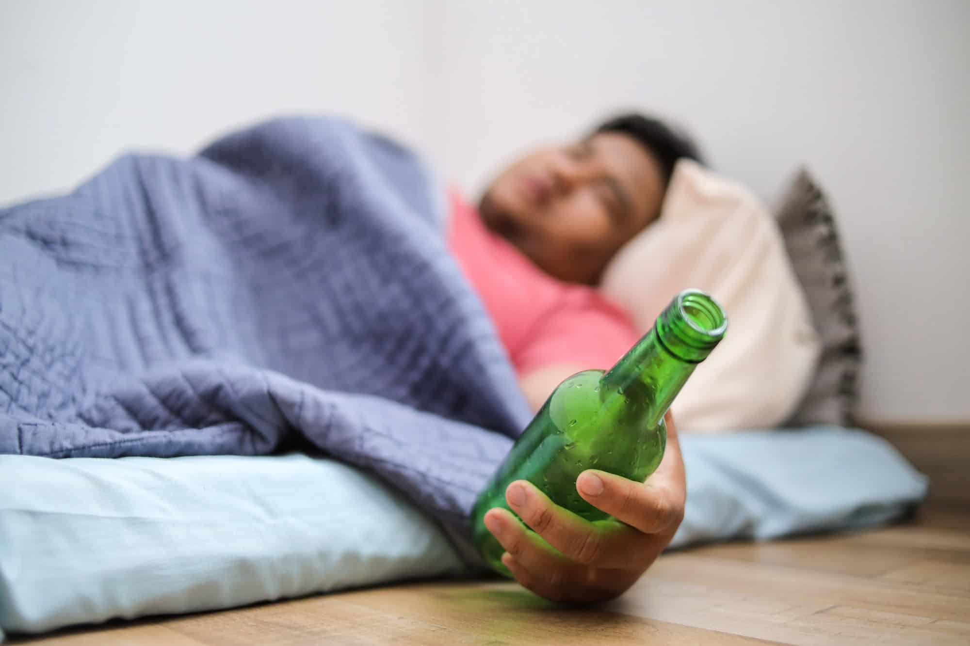 Pessoa dorme na cama segurando uma garrafa de bebida alcoólica
