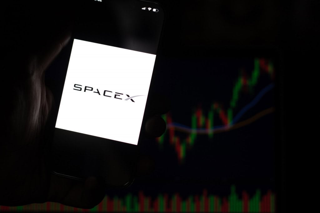 Ao fundo, gráficos financeiros; à frente, logo da SpaceX