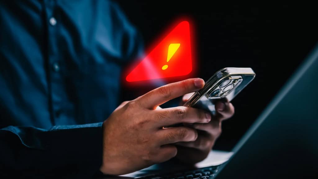 Pessoa usando iPhone com símbolo de alerta de segurança em cima do celular