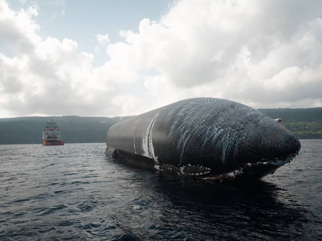 Starship parcialmente submersa no oceano, com o escudo térmico danificado, enquanto um navio de apoio se aproxima ao fundo – Crédito: SpaceX/Reprodução/X