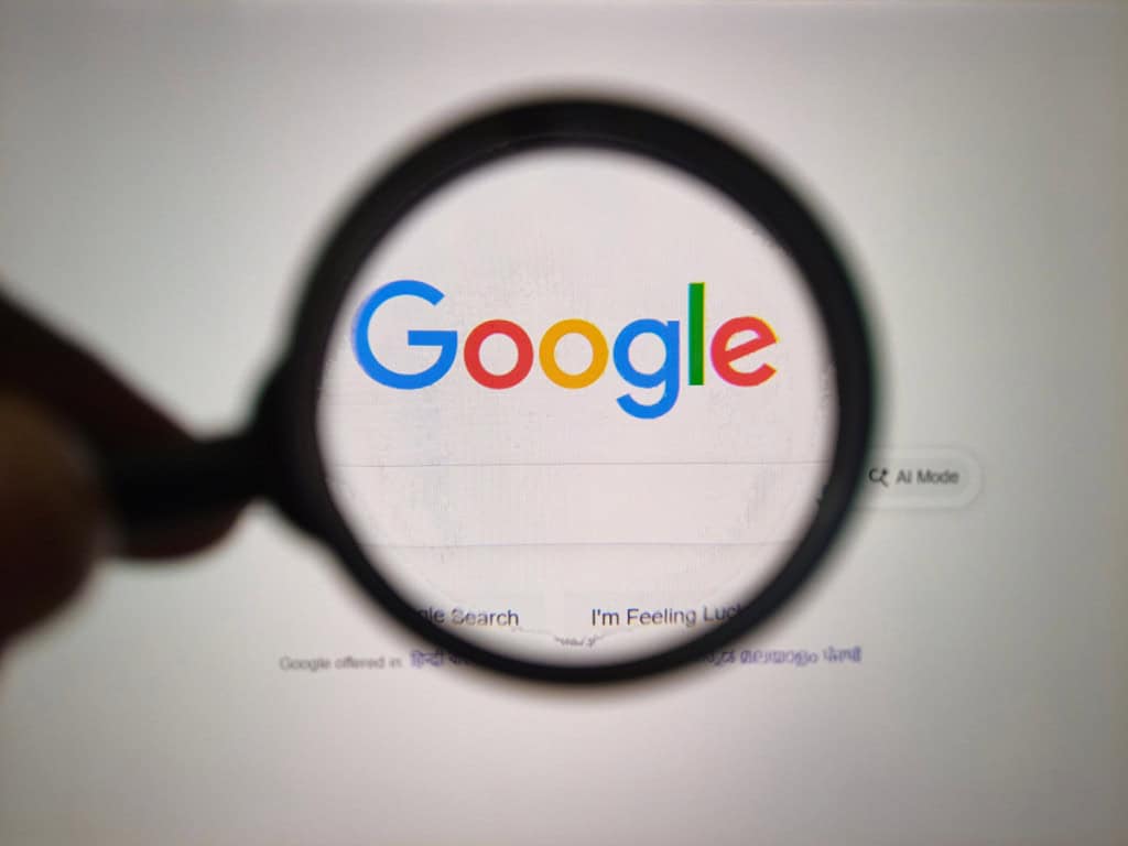 Sala 9 Google testa remuneração para sites que ajudam suas ferramentas de IA a gerar respostas mais úteis 3 Um close-up de uma lente de aumento segurada sobre o logotipo icônico do Google exibido em um monitor de computador, destacando o poder da pesquisa.