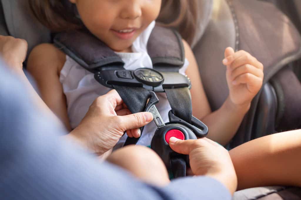 Close de uma pessoa colocando uma criança em uma cadeirinha
