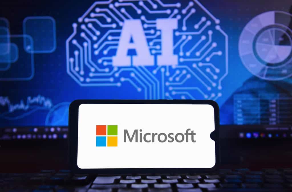 Sala 9 Microsoft quer transformar o Windows em um sistema operacional de IA 2 Logo da Microsoft exibido em um notebook diante de uma tela com elementos gráficos relacionados à inteligência artificial.