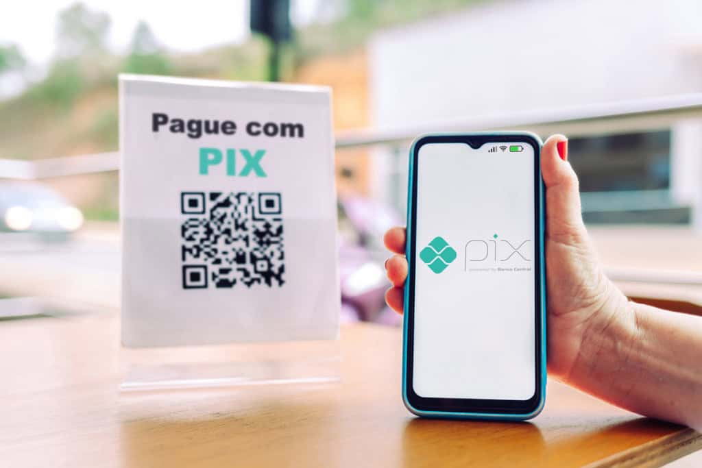 mão segurando um smartphone e escaneando um QR code em um suporte de acrílico para pagamento via PIX