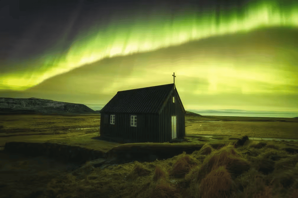 Aurora boreal ao fundo com uma casa mais à frente