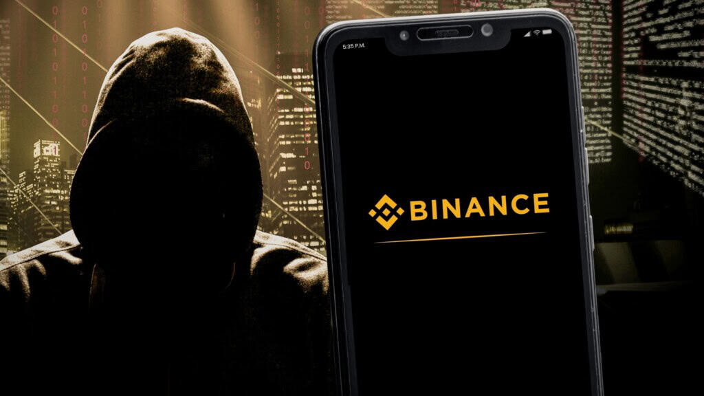 Montagem de hacker atrás de celular exibindo logomarca da Binance