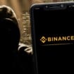 Montagem de hacker atrás de celular exibindo logomarca da Binance